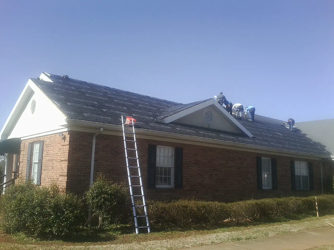 Crew tearing shingles off a brick ranch roof with a ladder set — Metal Roof Repair work by our crew in Cumming