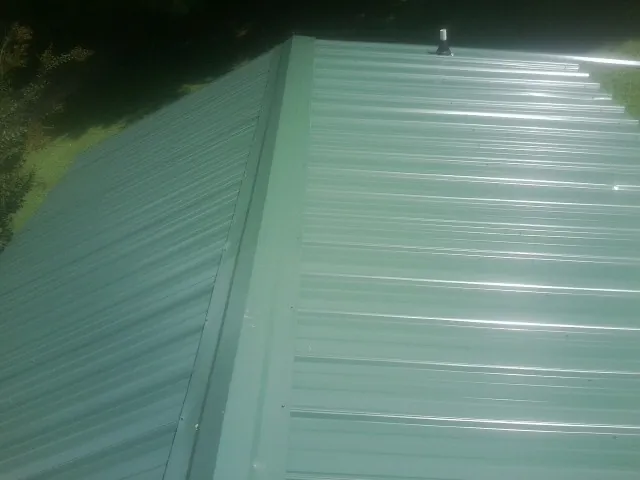 New green metal panels meeting at the ridge of a roof — Flat Roof Repair work by our crew in Cumming