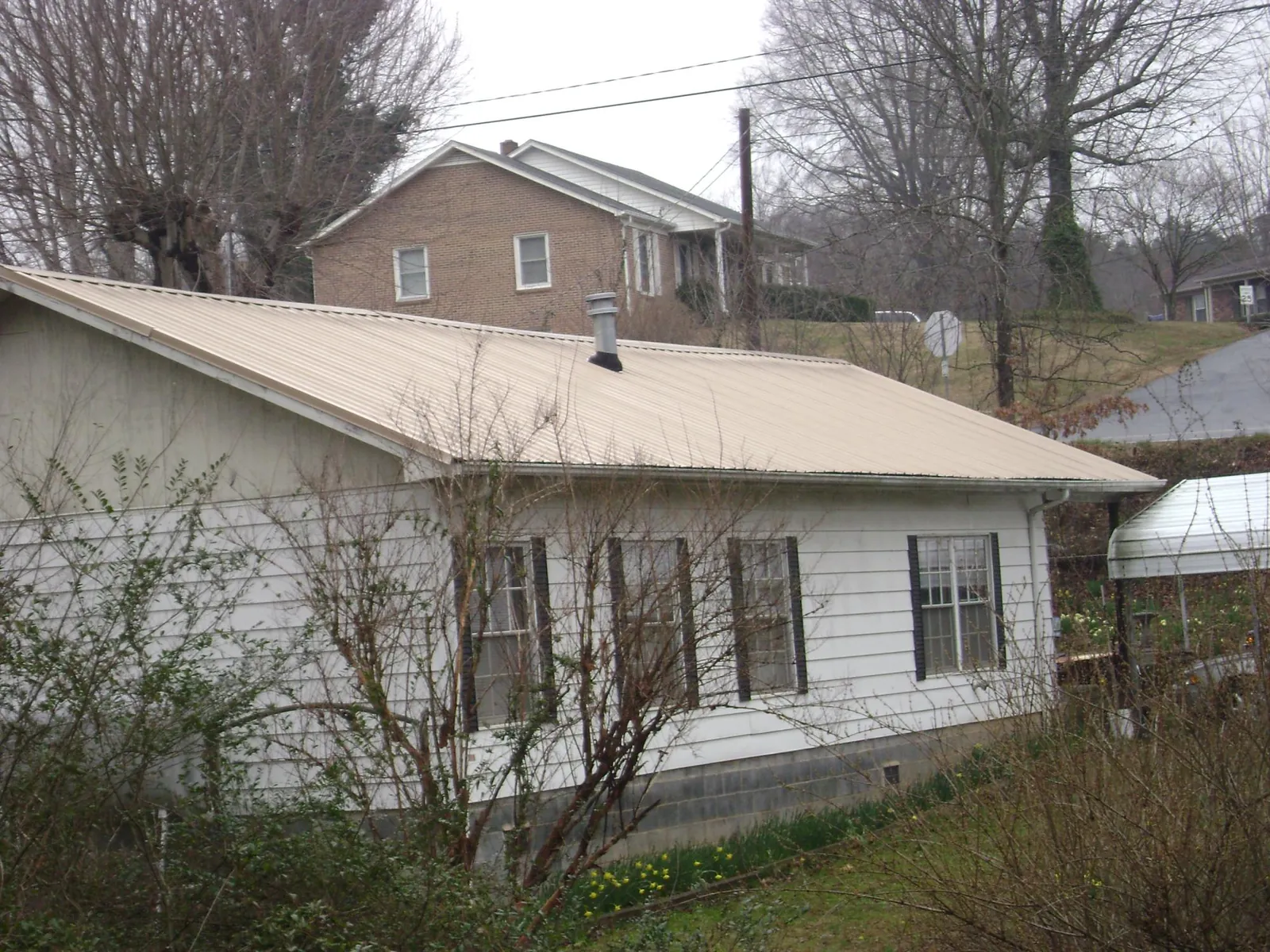 Tan metal roof on a white sided house set into a hillside — Commercial Roofing by Roofing Brothers in Cumming